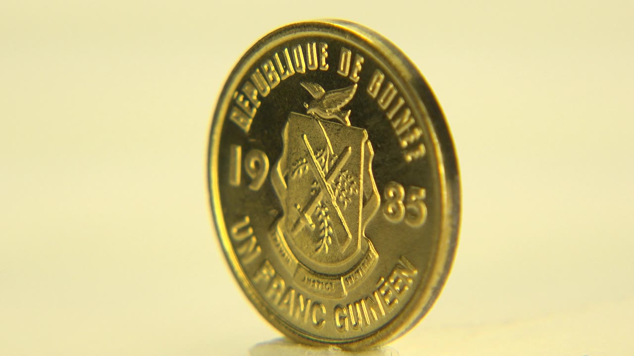 Gold-colored coin standing on edge against a yellow background.