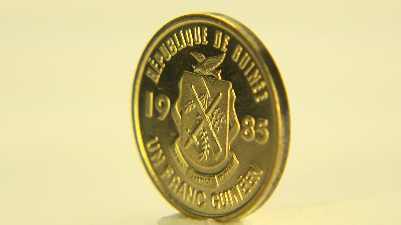 The coin remains upright in Westminster, Colorado and turns slightly toward the camera, with warm yellow light and no visible people.
