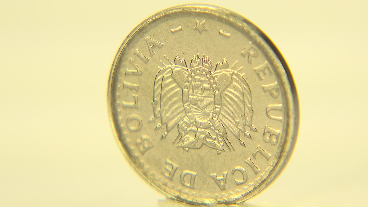 Close view in Westminster, Colorado of an upright gold-toned coin showing the Bolivian crest side against a pale yellow background, with no visible people.