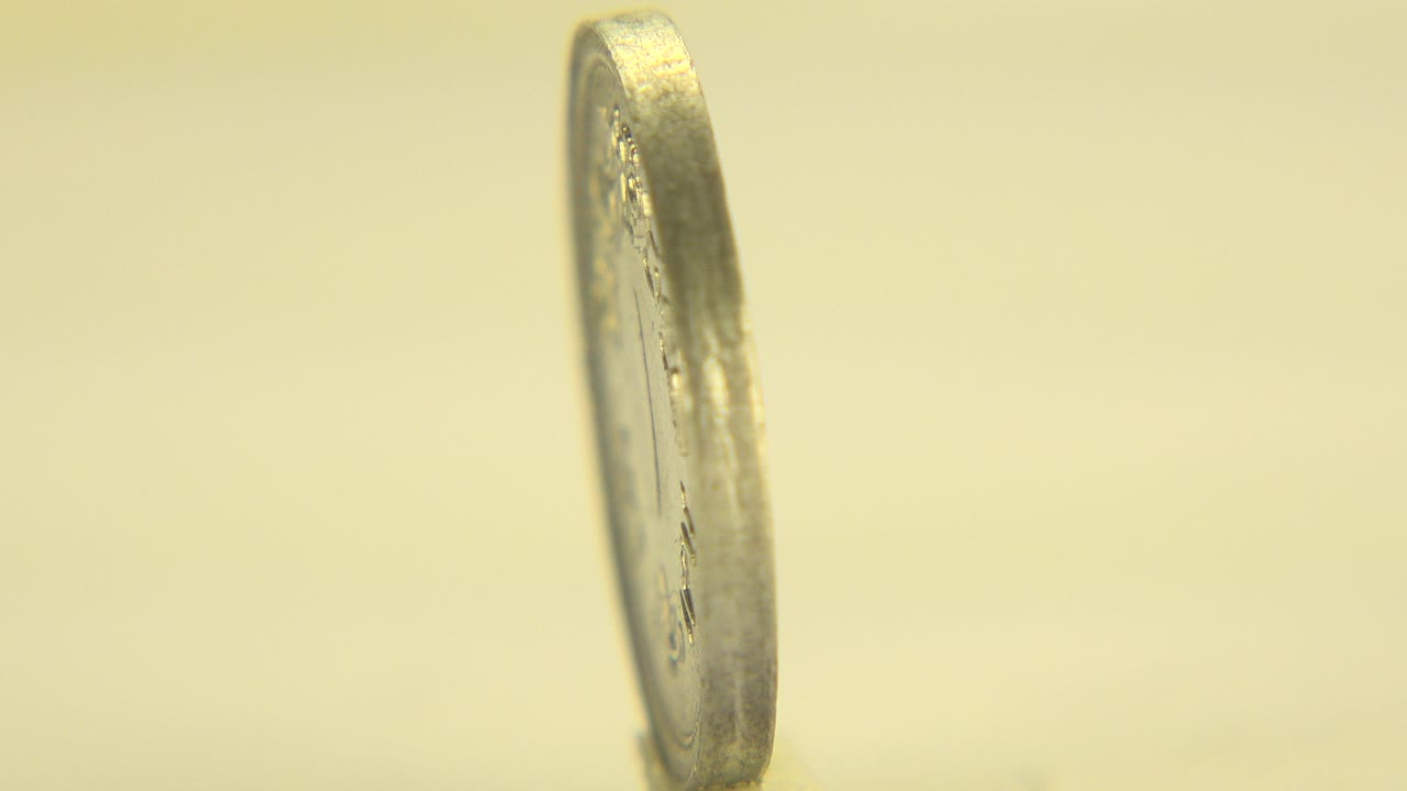 Thin coin standing upright above a blurred coin face