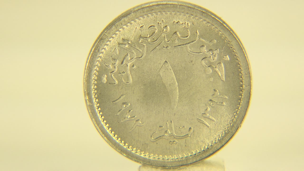 The coin remains mostly face-on and centered, with warm light reflecting across its worn metallic surface and no visible people.