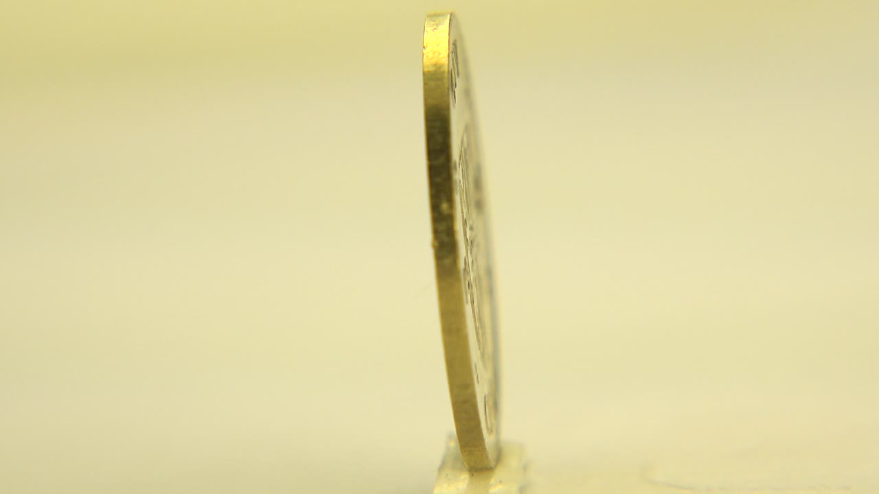 The coin remains mostly edge-on, upright on the tabletop with a faint contact point visible below it and no visible people.