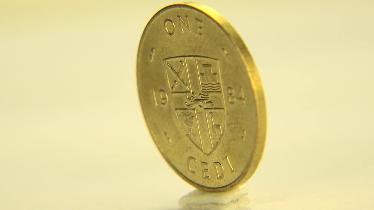 Gold-colored Ghana coin upright on a reflective surface in Westminster, Colorado, showing the one cedi face in warm light with no visible people.