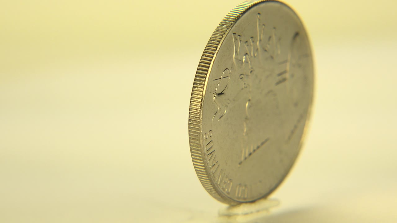 A silver coin stands nearly edge-on on a pale tabletop in Westminster, Colorado, with warm soft focus and no visible people.