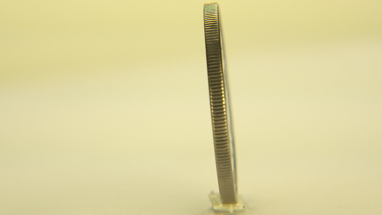Close tabletop view of the coin still mostly edge-on, with its ridged rim sharp against the warm background and no visible people in this frame.
