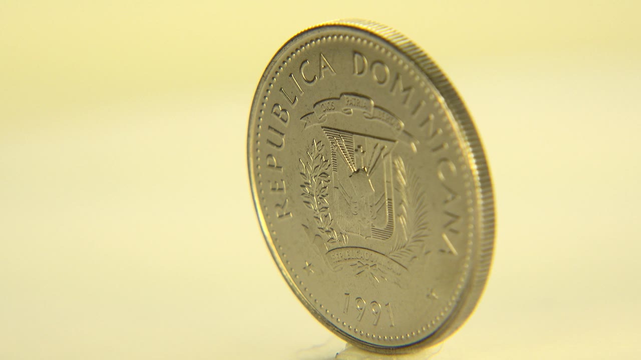 Gold-colored Dominican Republic coin stands upright at a slight angle on a pale surface in Westminster, Colorado 2015 footage, with no visible people.
