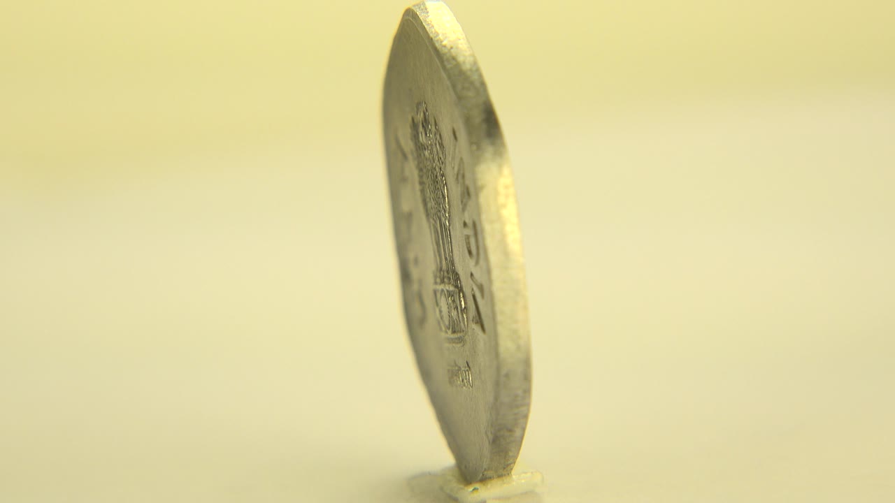 A bronze-colored coin stands nearly edge-on on a pale surface in Westminster, Colorado footage, with warm yellow light and no visible people.