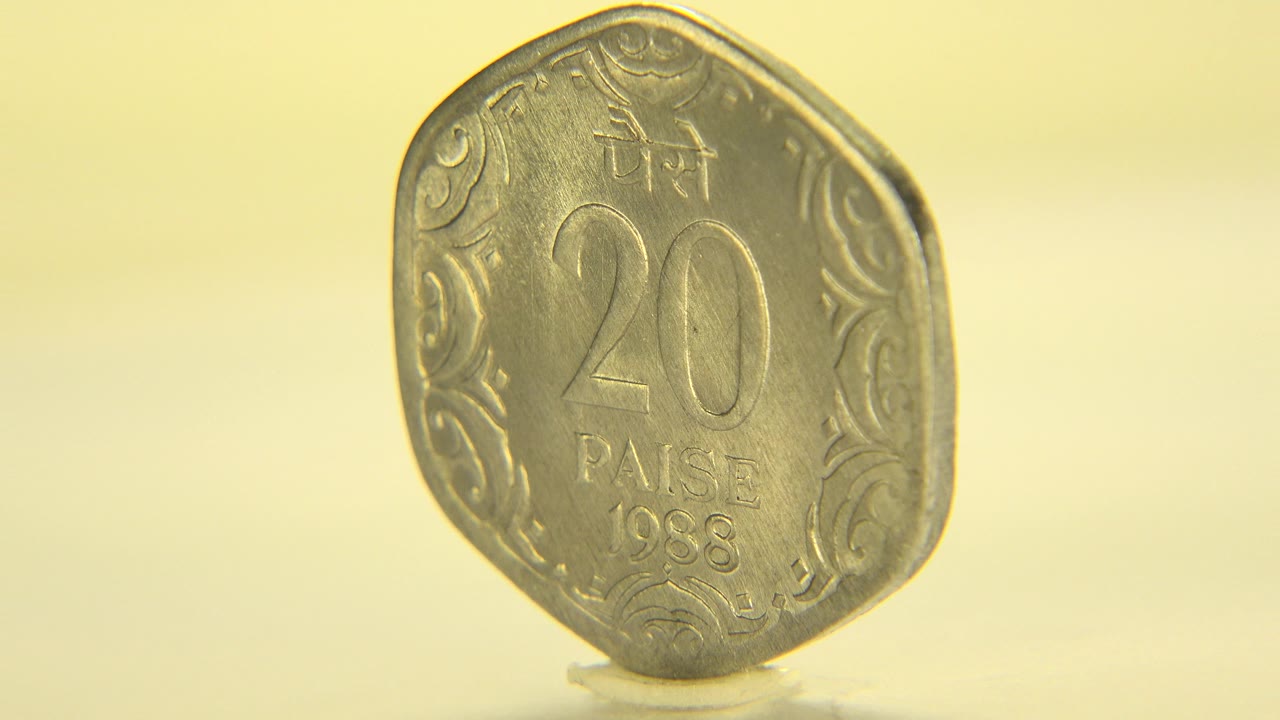 Indian 20 paise coin dated 1988 stands upright in close-up on a pale yellow surface in Westminster, Colorado, with no visible people.