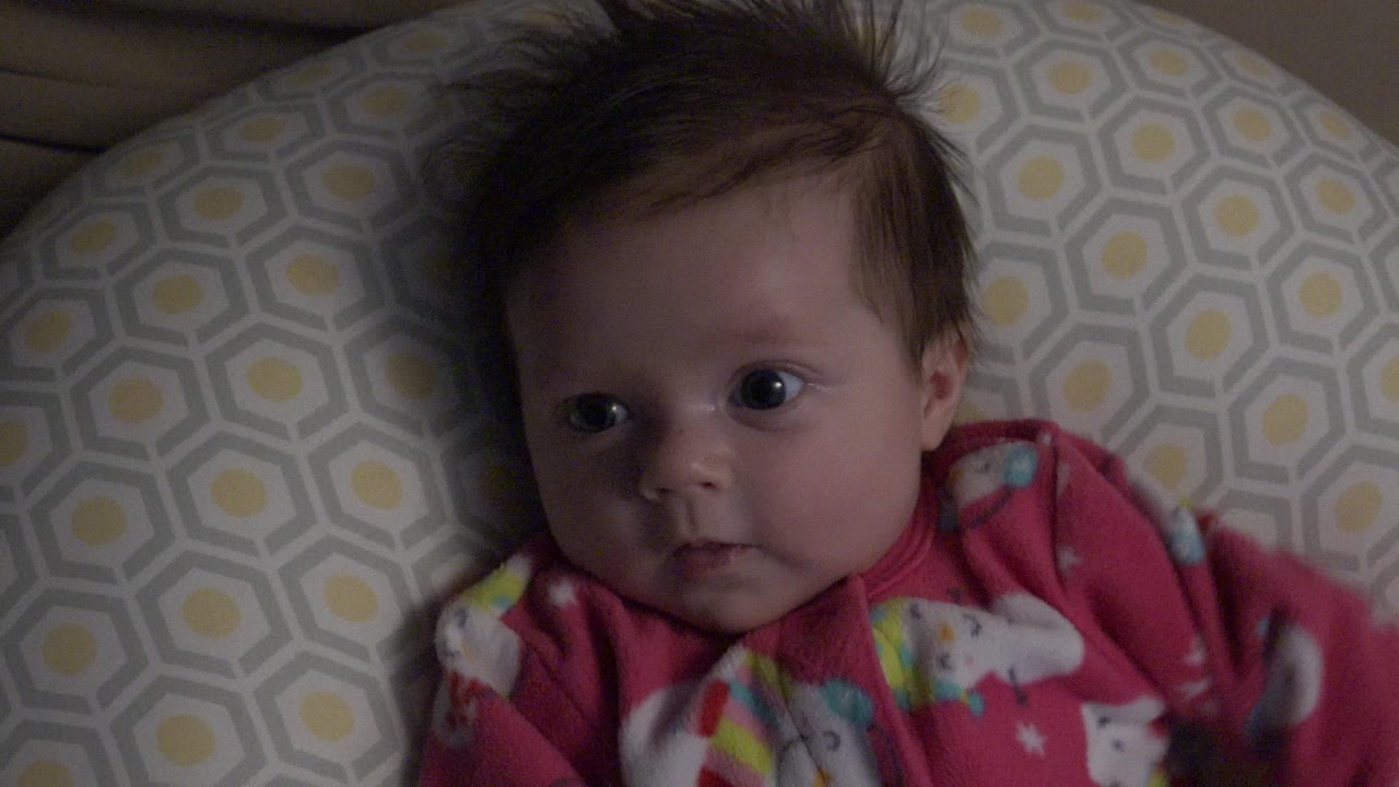 Baby girl lying on a patterned pillow in a pink outfit.