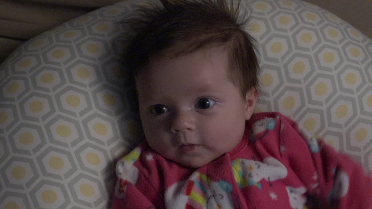 At 0:01, the baby girl remains on the patterned pillow in Westminster, Colorado, with wide eyes and her pink outfit visible across the lower frame.