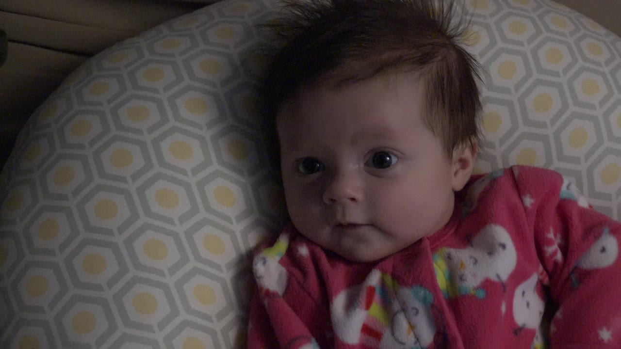 Baby boy lying on a patterned pillow in dim indoor light.