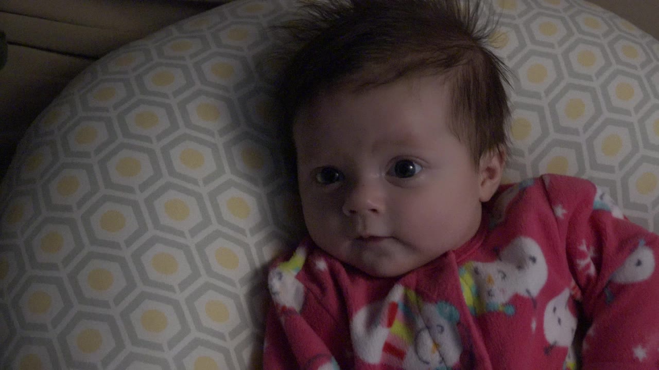 At 0:01, the baby boy remains close to the lens with wide eyes open, framed against the same gray and yellow pillow inside the Westminster, Colorado home setting.