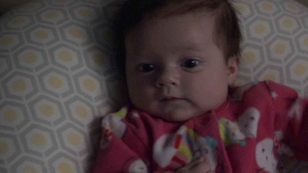 Baby in red pajamas lying against geometric bedding.