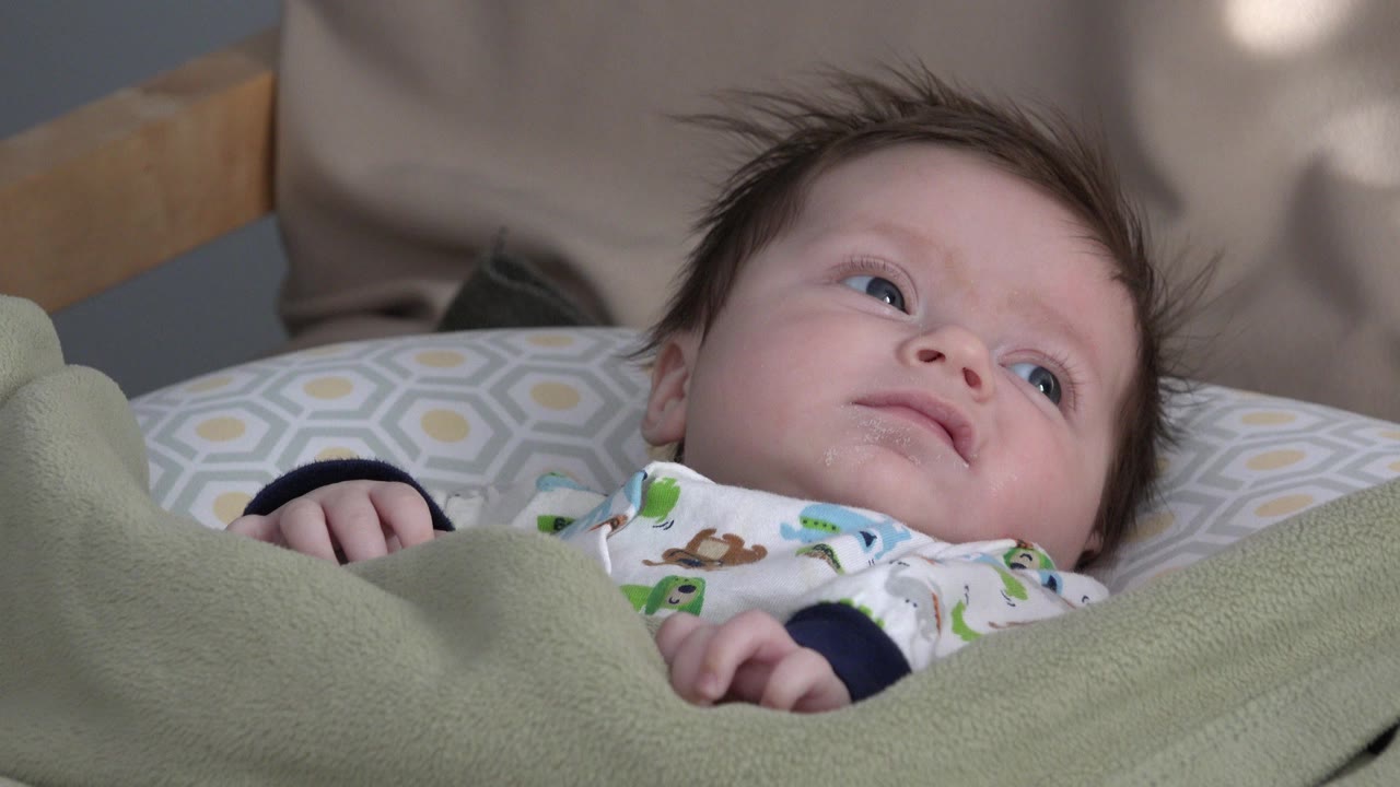 Baby boy lying under a green blanket and looking upward.
