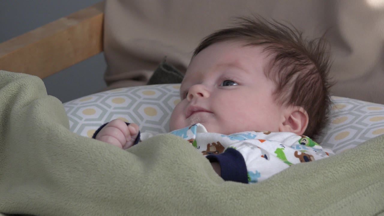 Baby lying on a pillow under a green blanket in a crib.