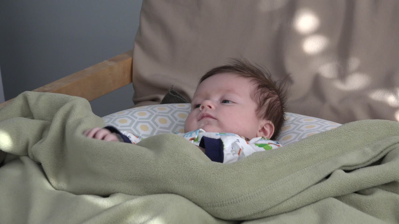 Baby lying under a green blanket in a crib.