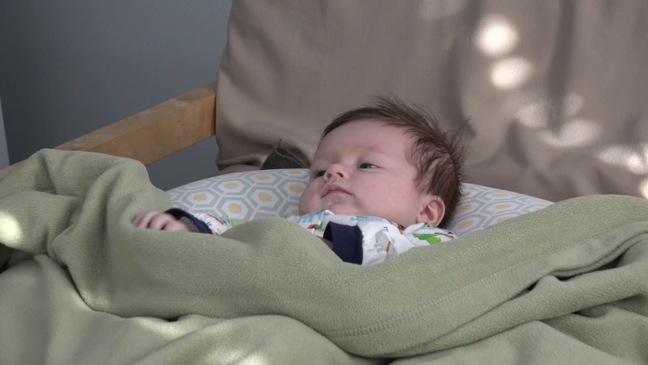 The baby remains reclined beneath the green blanket in Westminster, Colorado, with one small arm visible near the left side of the bedding.