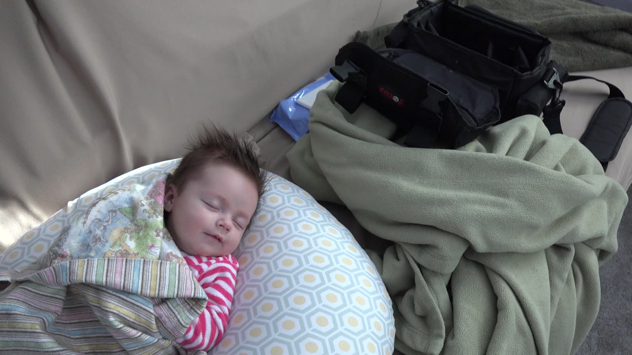 The baby remains asleep on the hexagon-patterned pillow in Westminster, Colorado, with the striped blanket across the body and a green fleece blanket bunched to the right.