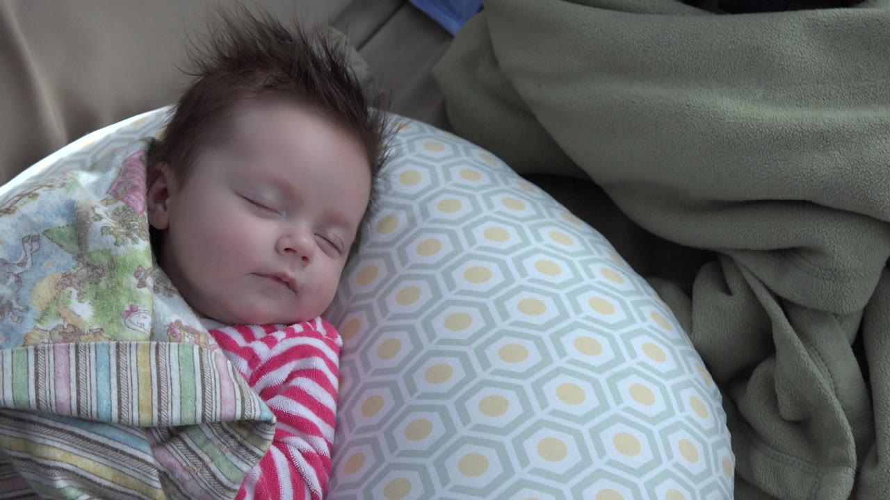 In Westminster, Colorado, a sleeping baby rests beside a yellow and gray patterned pillow with a green blanket and striped bedding partly covering the body.
