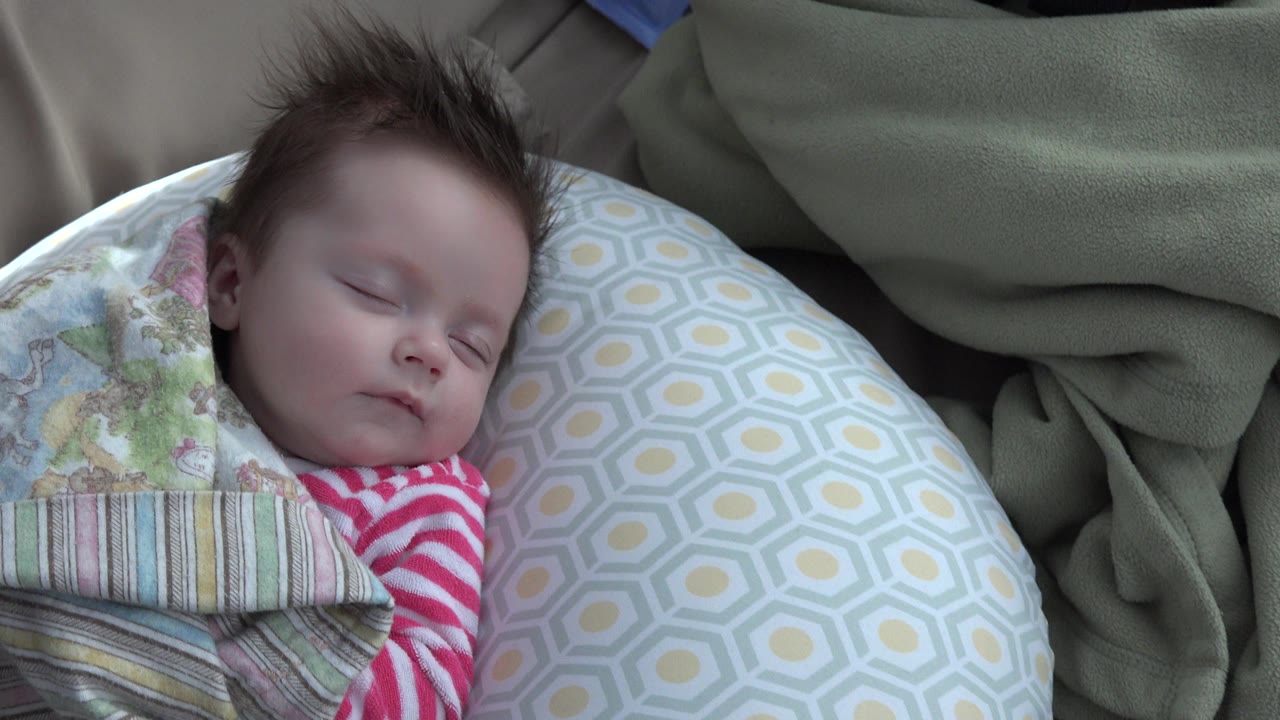 In Westminster, Colorado, the baby's closed face and red and white striped sleeve sit close to the patterned pillow, with green blanket fabric in the background.