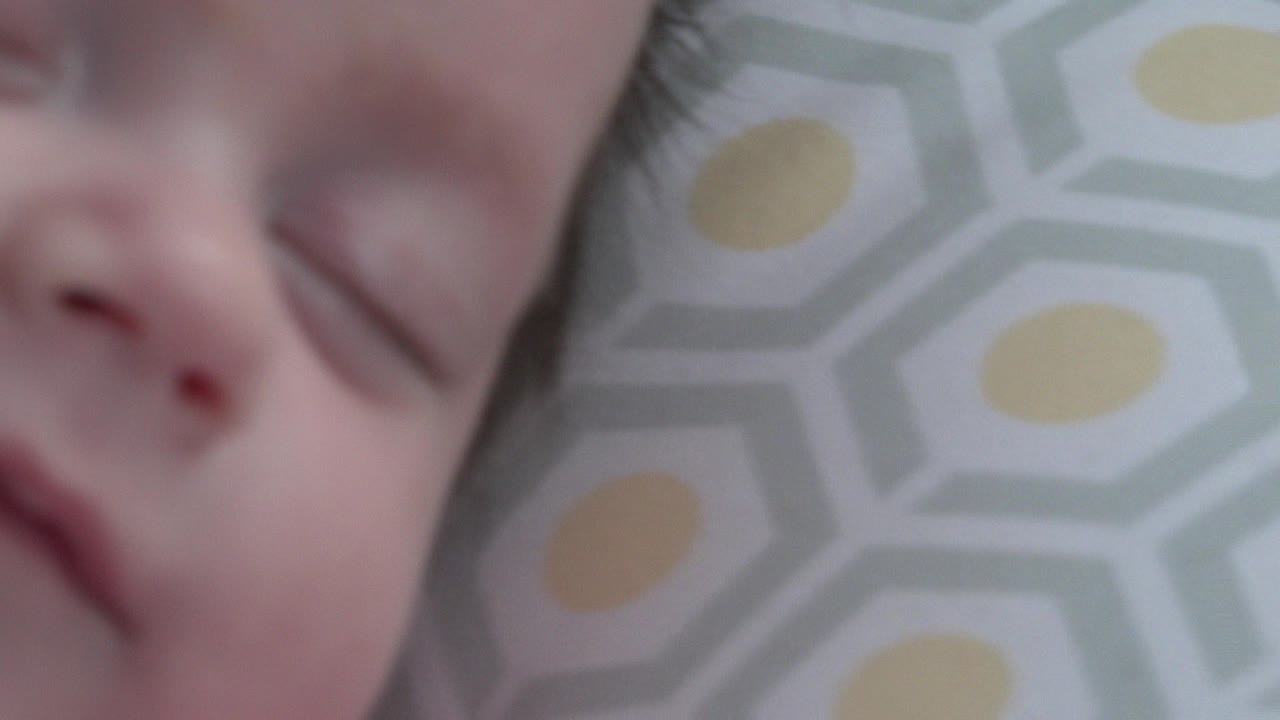 Close-up of a sleepy baby's face beside a patterned blanket.