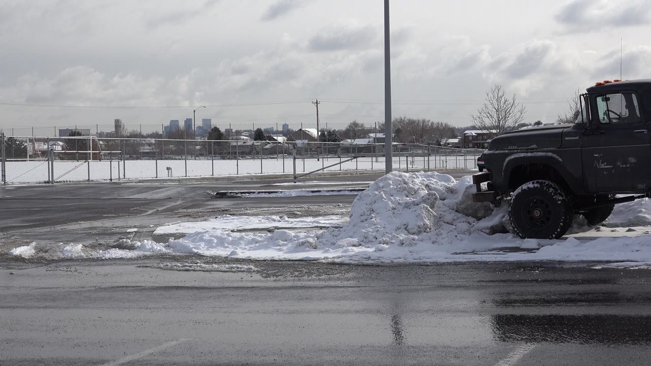 Dark truck partly behind a snowbank on a wet winter street.