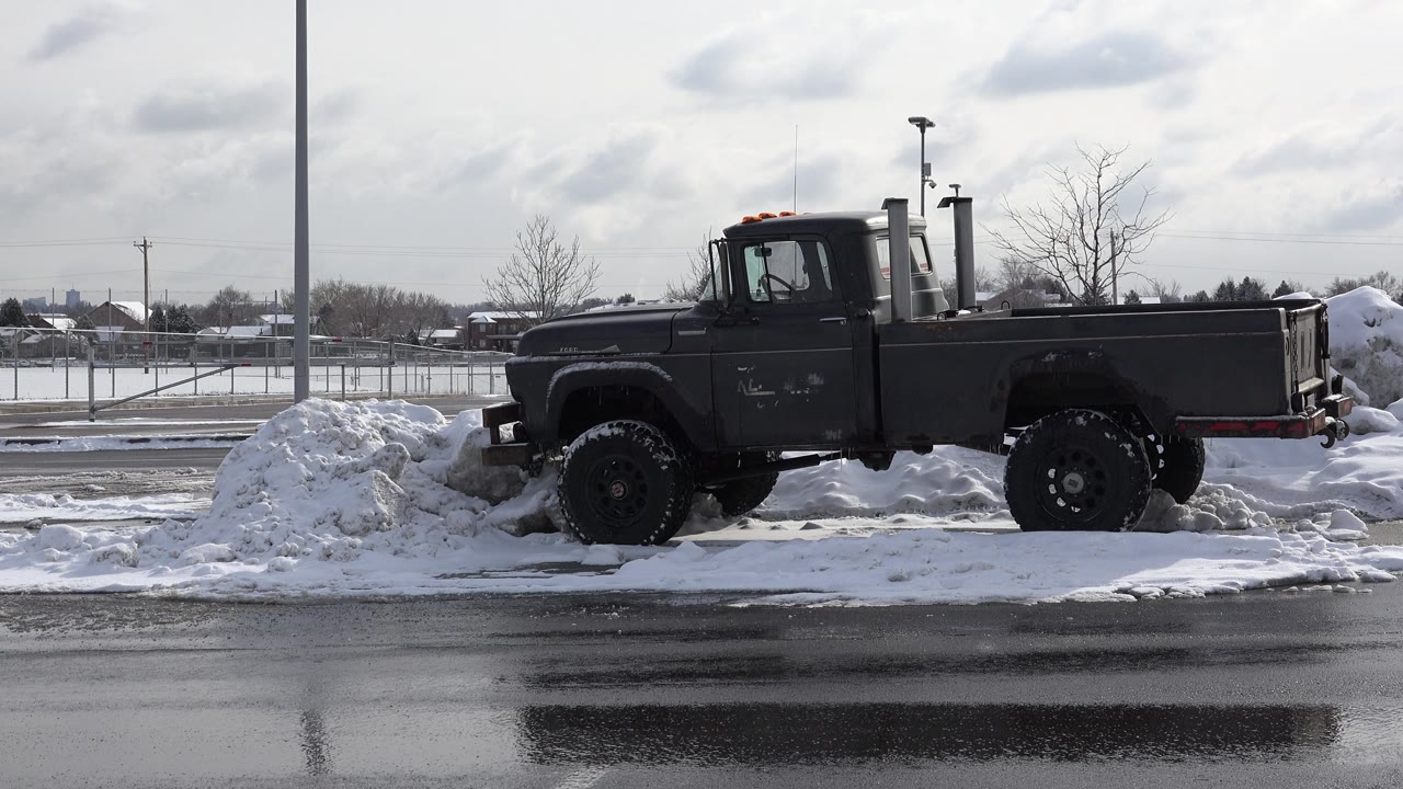 Dark parked truck with snow piled around the tires.