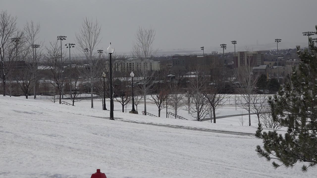 Wide Westminster, Colorado winter view with a snow-covered slope, bare trees, field lights, distant buildings, and no clearly visible people at the start of the clip.