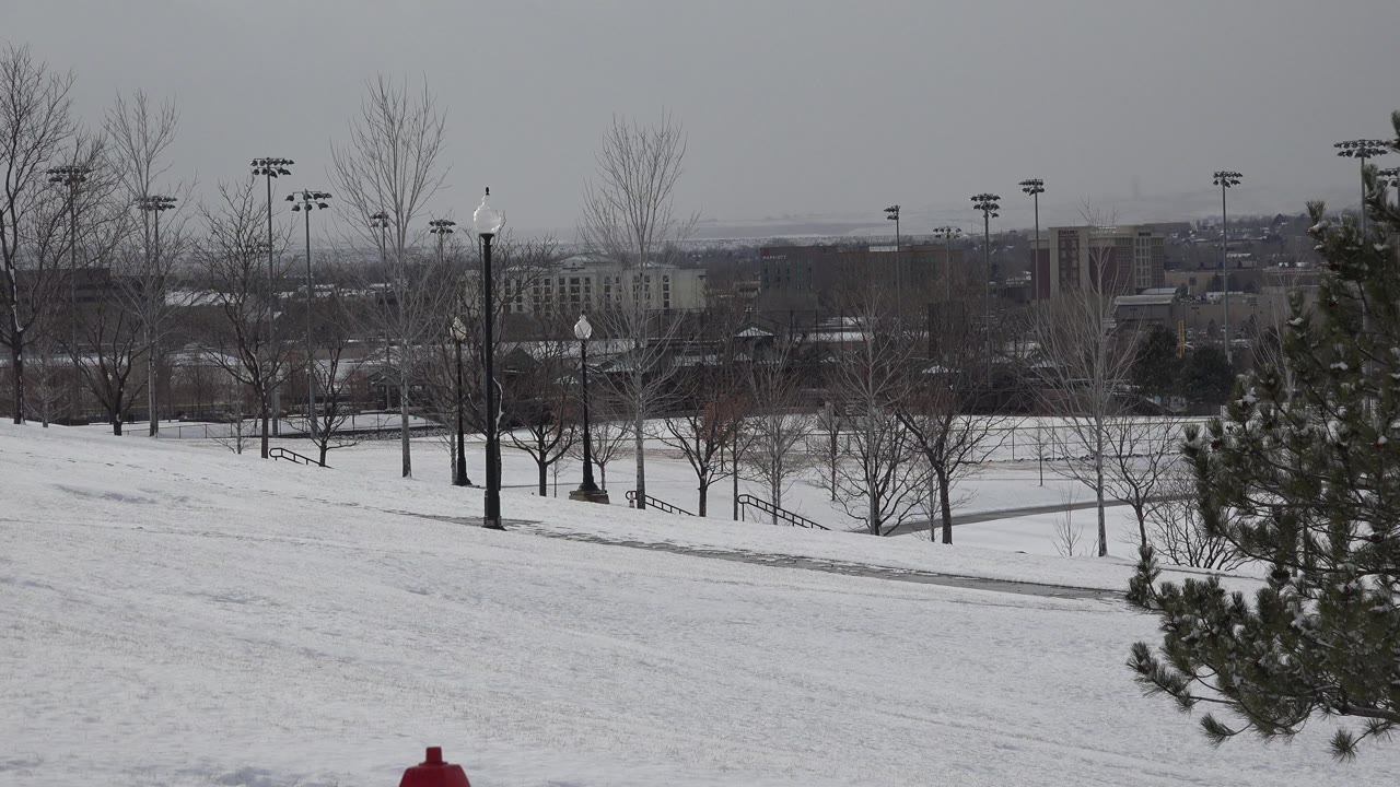 Westminster, Colorado sports grounds sit under snow with leafless trees, tall field lights, a hazy skyline, and no clearly visible people one second into the clip.
