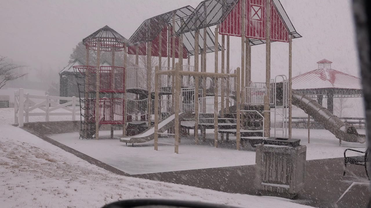 At 0:00, a red and tan playground or amusement-park structure stands in falling snow in Westminster, Colorado, with a trash can in the foreground and no visible people.