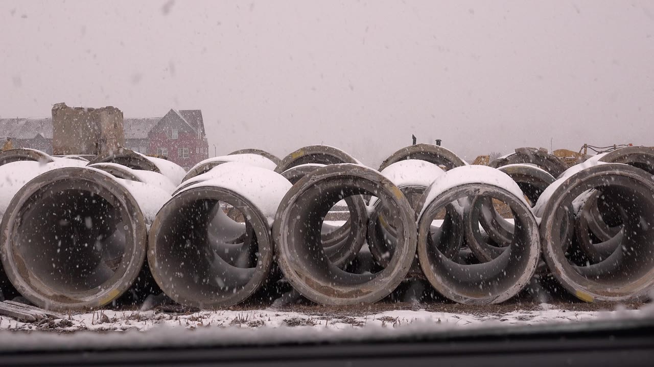 Rows of concrete pipes during a snowy worksite day