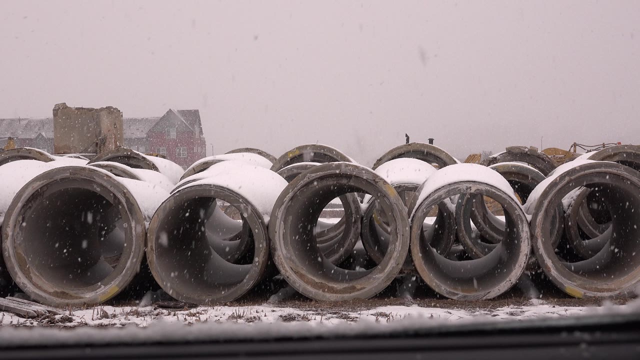 Snow-covered concrete pipe segments stacked in a yard