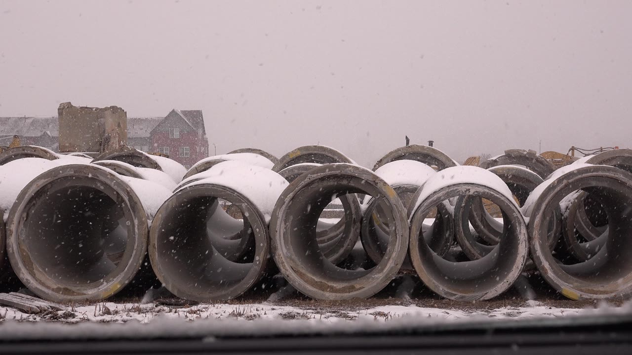 Snow-covered concrete pipe sections stacked in an outdoor yard.