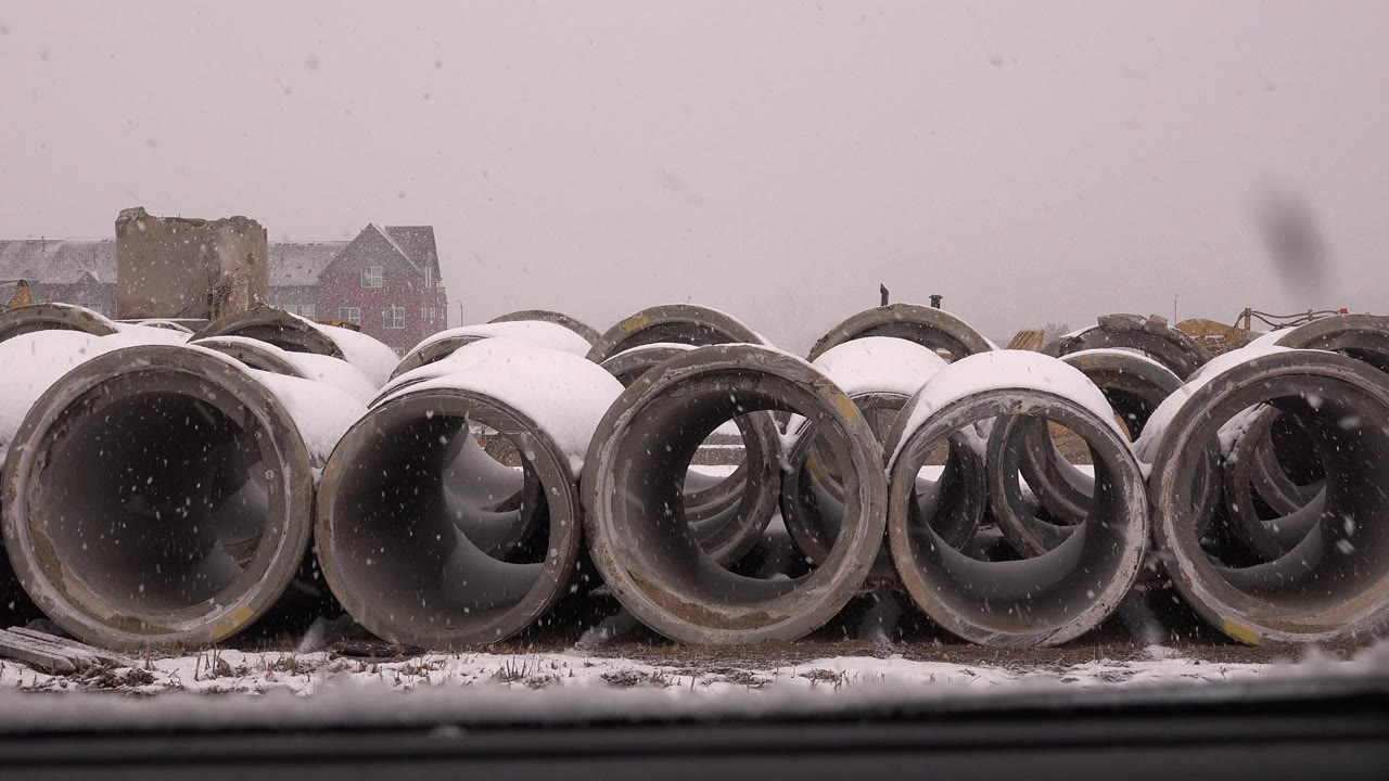 A row of concrete pipe openings fills the frame in Westminster, Colorado, with white snow on the pipe tops, a dark road strip below, and no visible people.