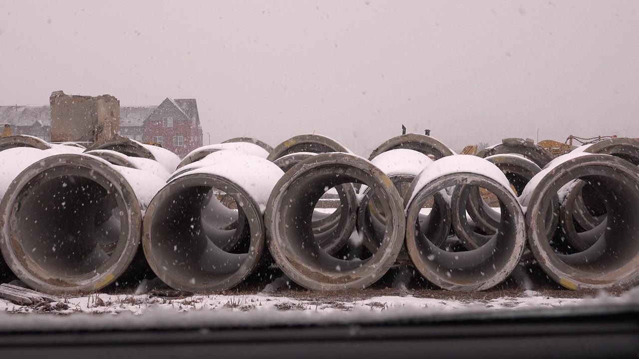 Snow-covered concrete pipes beside dark foreground rails