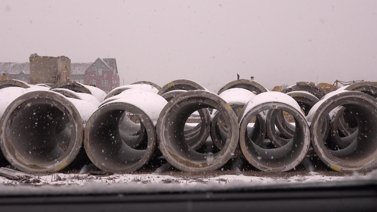 The second frame holds on snow-dusted concrete pipe openings in Westminster, Colorado, with faint buildings in the background and no visible people.