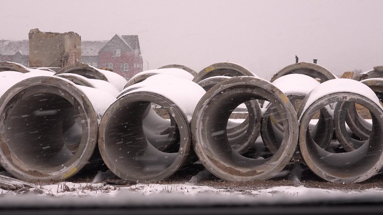 Snow-covered concrete pipe sections in a winter yard.