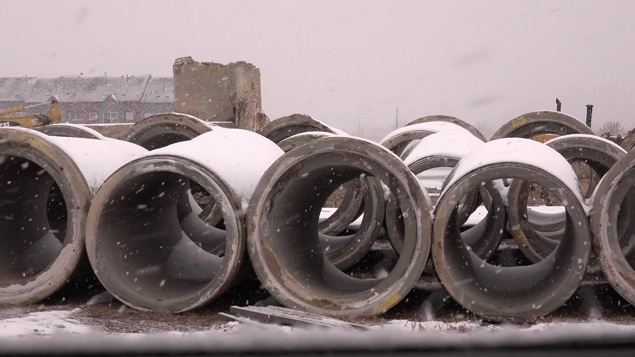 Large round concrete pipes dominate the frame in Westminster, Colorado, with snow collecting on the rims and no visible people.