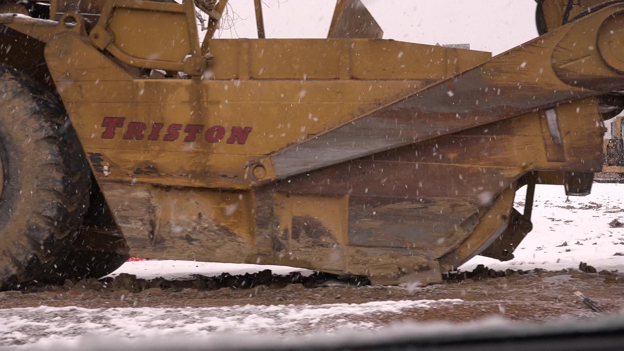 Close view of a yellow scraper tractor in falling snow.