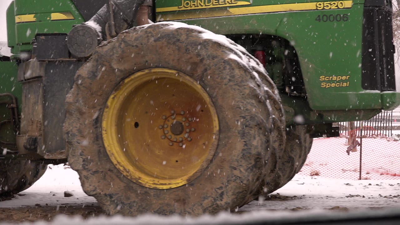Close-up of a muddy tractor tire in falling snow.
