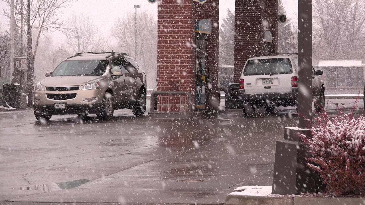 Beige crossover and minivan at a gas station in falling snow.