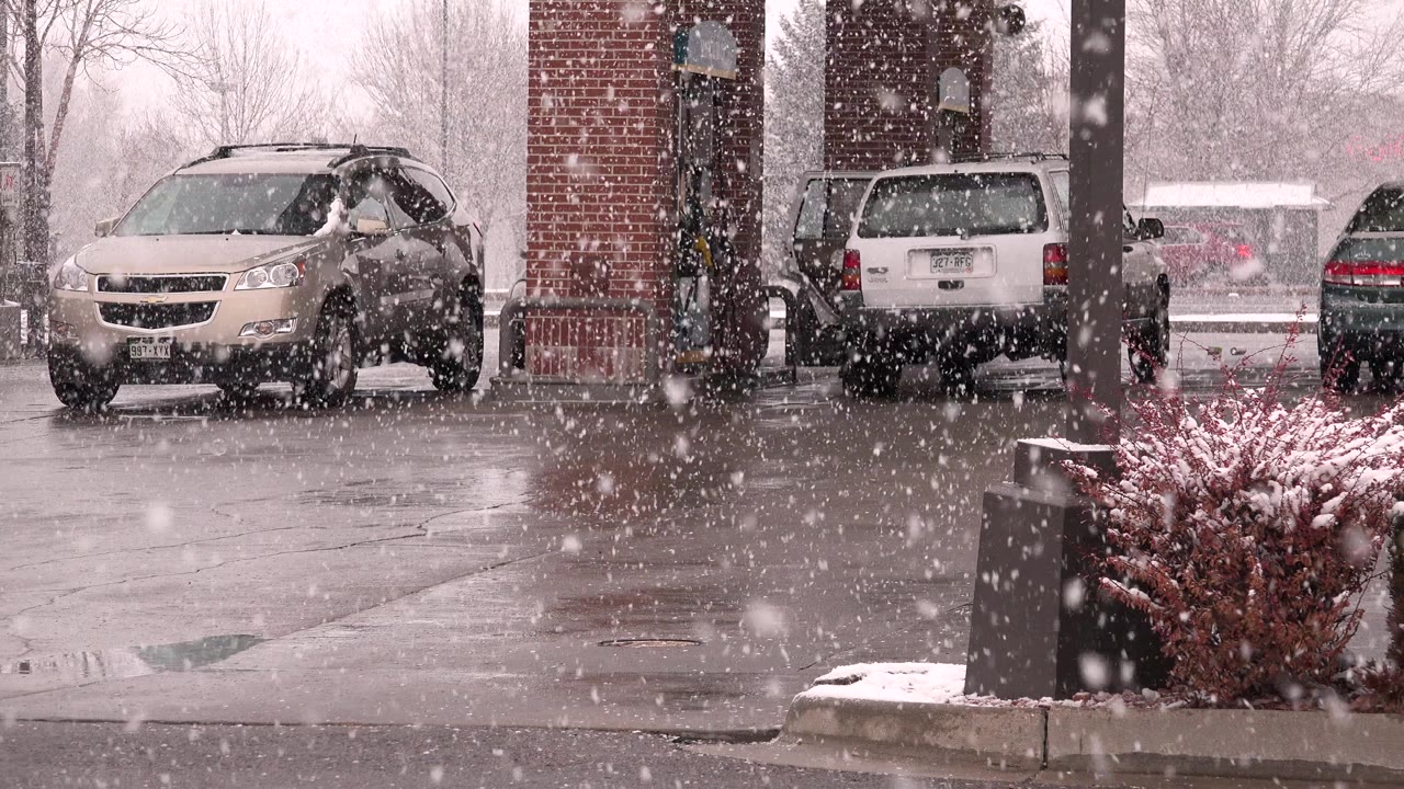 Snow falling over parked cars at a gas station.