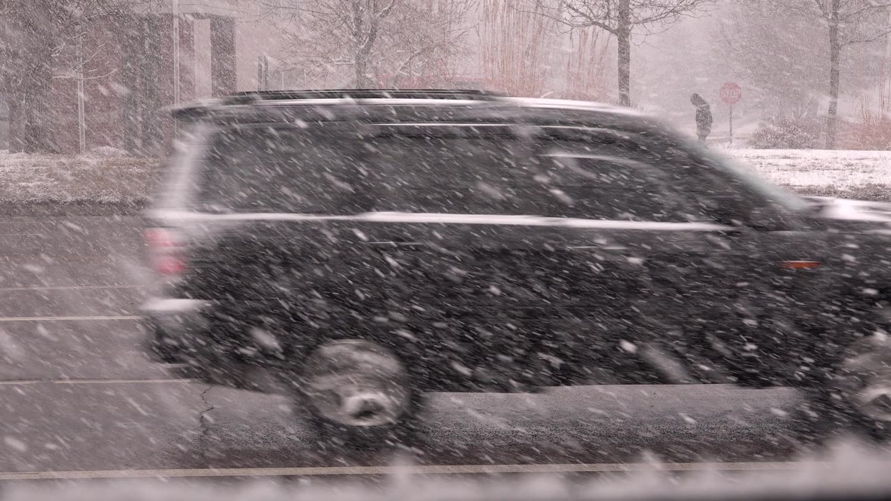Black SUV driving through heavy snow on a wet road.
