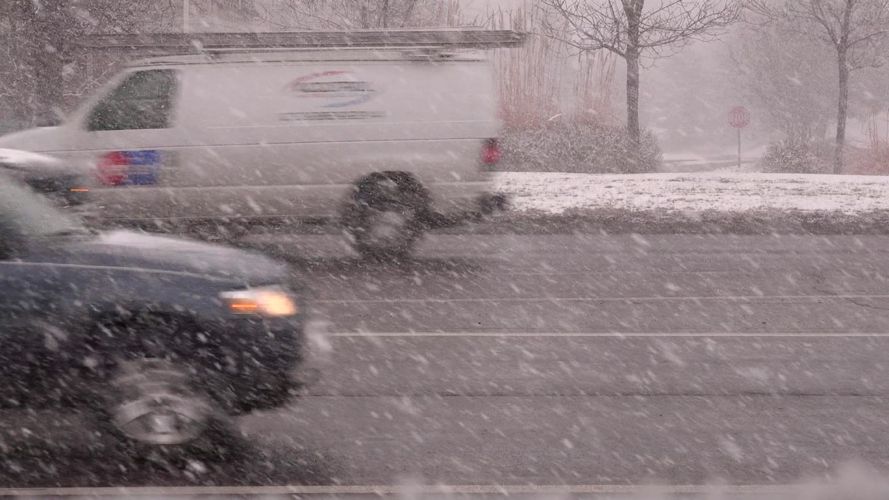 A dark SUV drives past in heavy snow with a headlight visible.