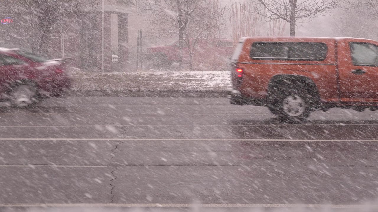 Dark red vehicle blurred by blowing snow on the road.