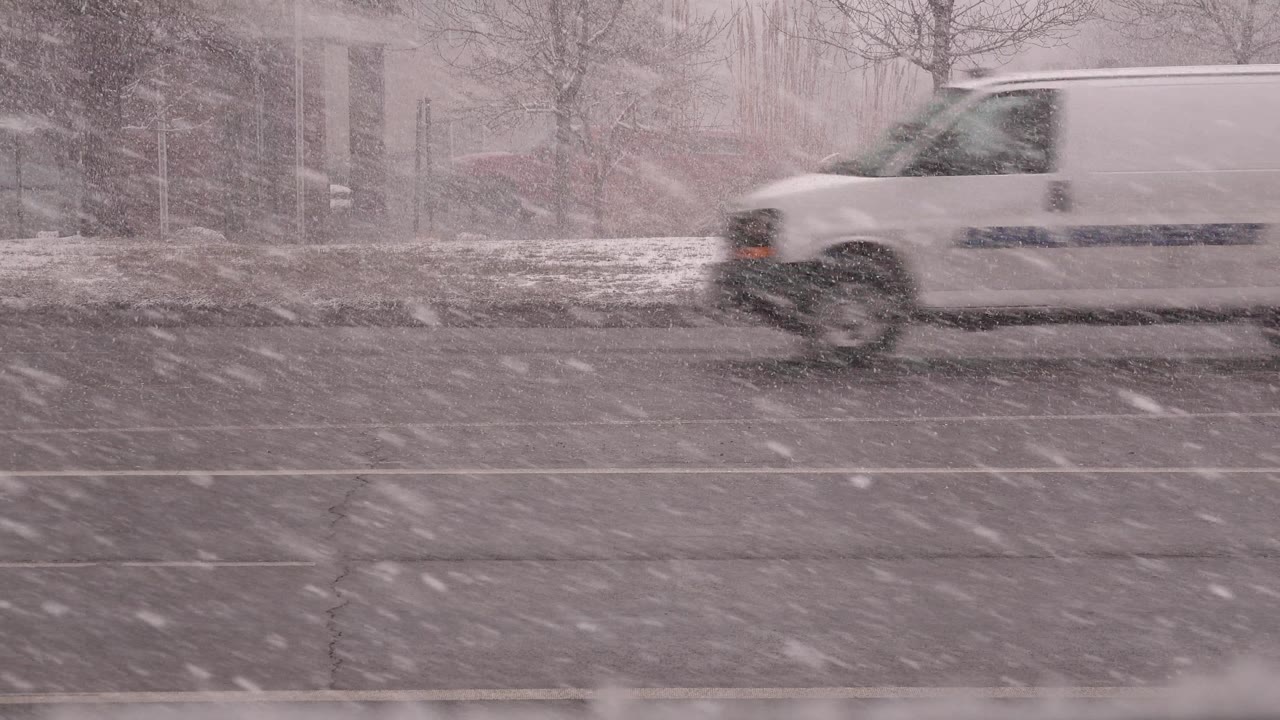 At 0:02, a white van moves through the right side of the Westminster, Colorado road scene as heavy snow reduces contrast and no visible people appear in the frame.