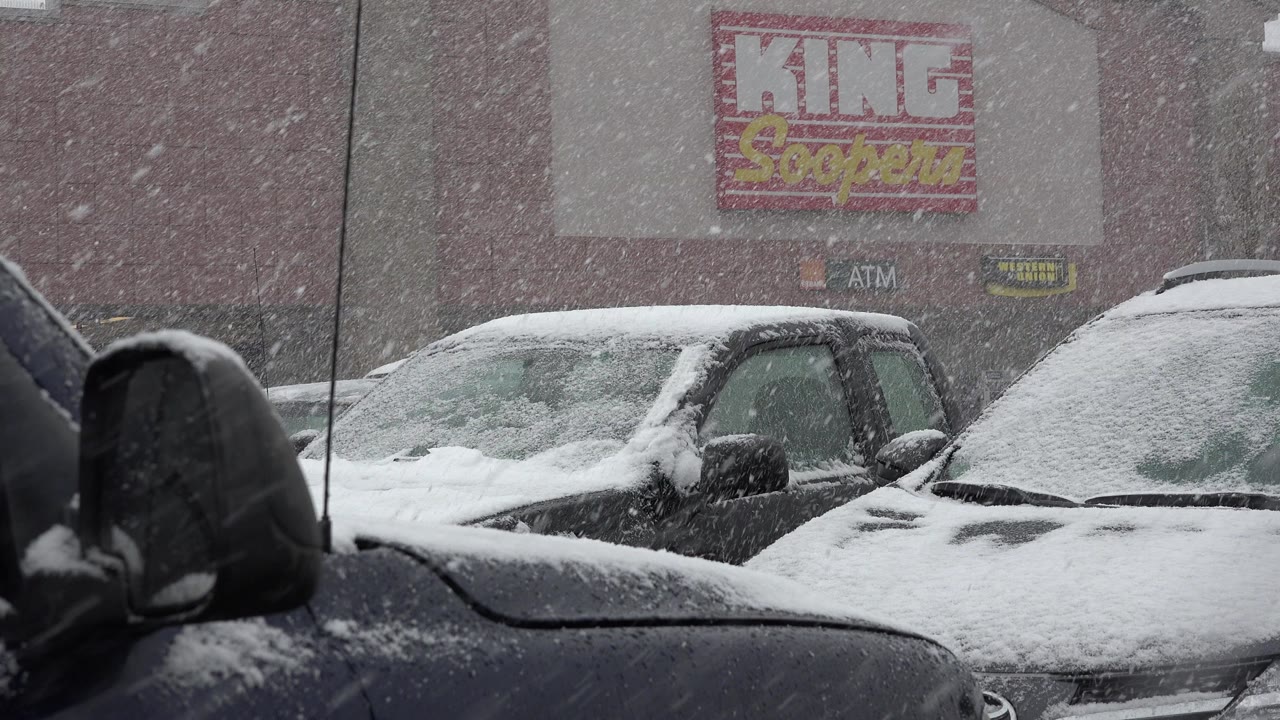 At 0:00, heavy snow falls over parked vehicles outside a King-branded storefront in Westminster, Colorado, with no visible people.