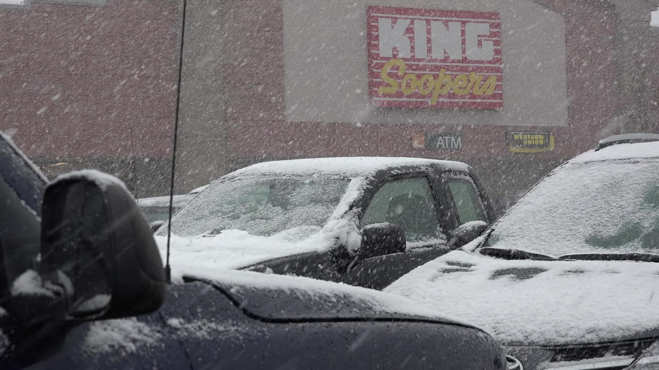 At 0:01, the same parking area remains framed tight on snow-capped vehicles, with King signage and ATM signage visible in the background and no visible people.