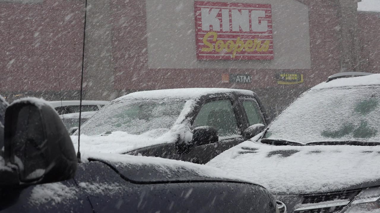 At 0:00, heavy snow falls over parked cars in a Westminster, Colorado store parking lot, with a King Soopers sign visible on the wall and no visible people.