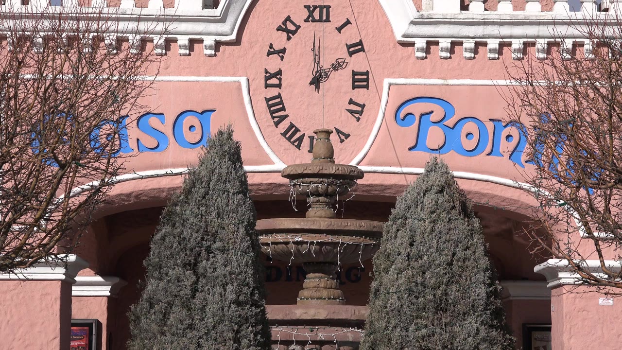 Pink building facade with painted clock, fountain, trees, and blue signage.